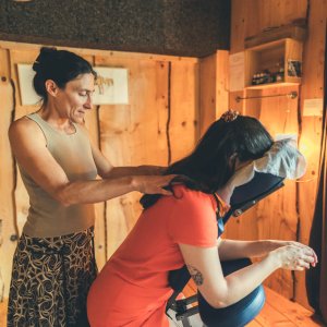Sarah masse les épaules d'une femme assise sur une chaise ergonomique dans son cabinet.