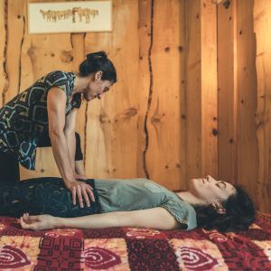 Durant un massage intuitif, Sarah a les mains posées sur les hanches d'une jeune femme allongée sur un futon.